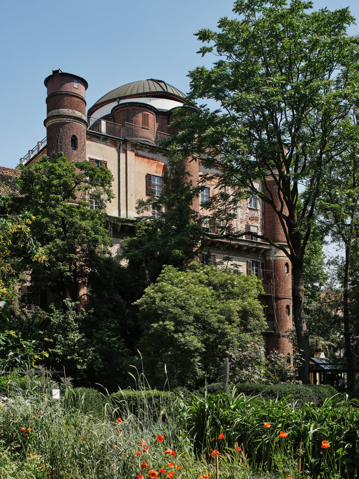 View of the Brera Observatory from the Orto Botanico in Palazzo di Brera with greenery and red flowers in the foreground 
