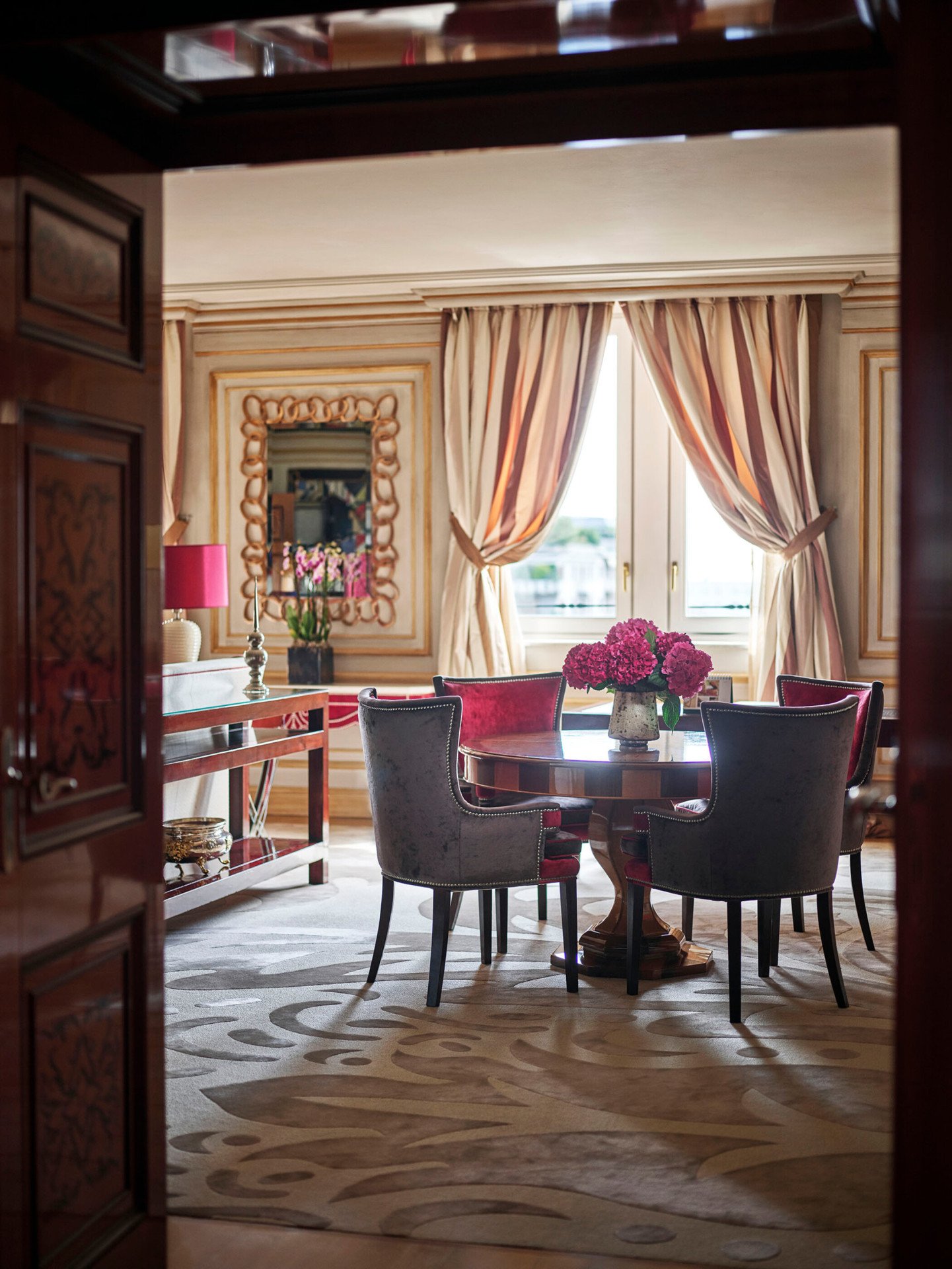 Soggiorno della Suite Executive arredato con un tavolo di legno, quattro sedie di velluto rosso e un bouquet di fiori rosa
