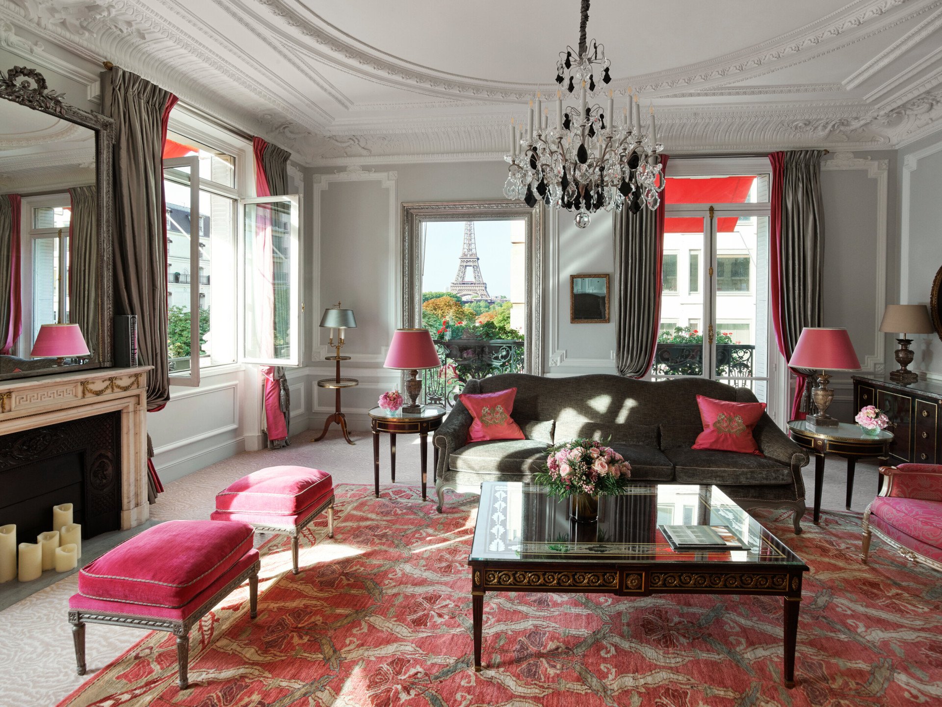 Élégant salon parisien à la décoration vintage, avec lustre, touches de rose et vue sur la tour Eiffel depuis les fenêtres ouvertes.