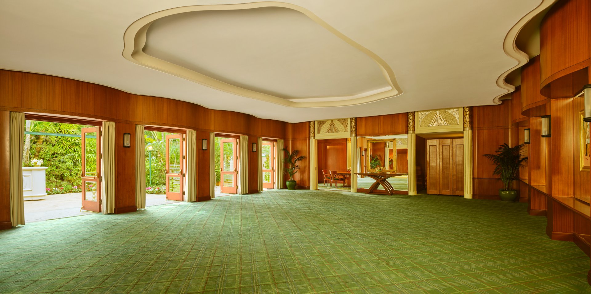 Spacious, empty event hall with large windows, green carpet, and wooden wall panels.
