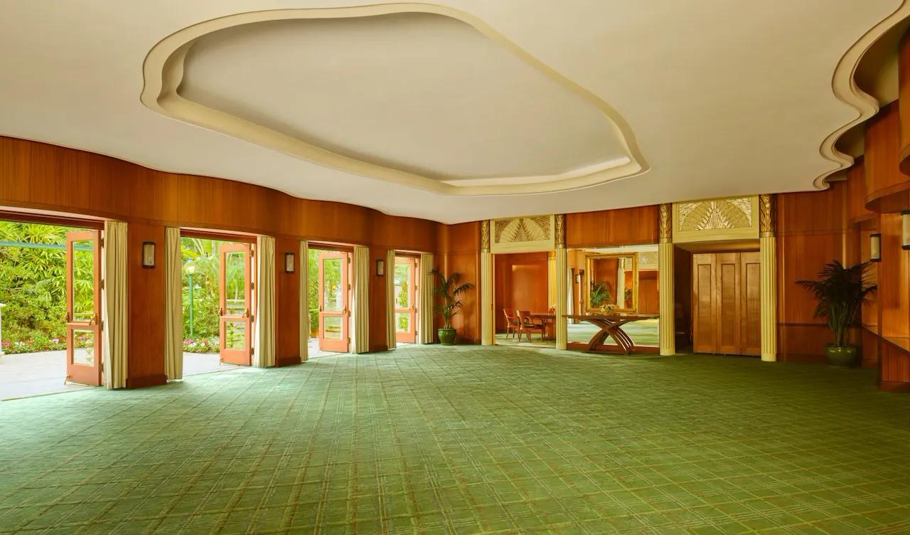 Spacious, empty event hall with large windows, green carpet, and wooden wall panels.