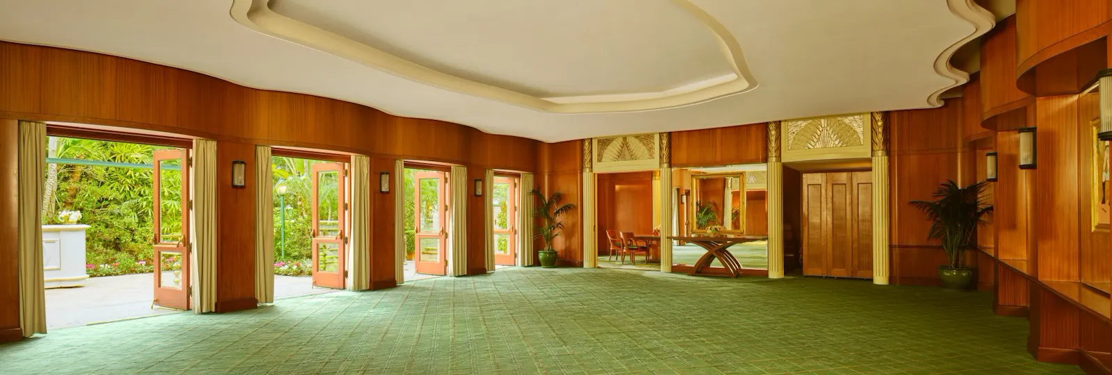 Spacious, empty event hall with large windows, green carpet, and wooden wall panels.