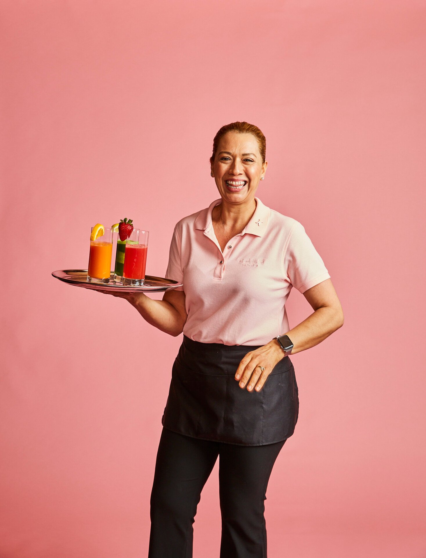 Woman holding three drinks against a pink background