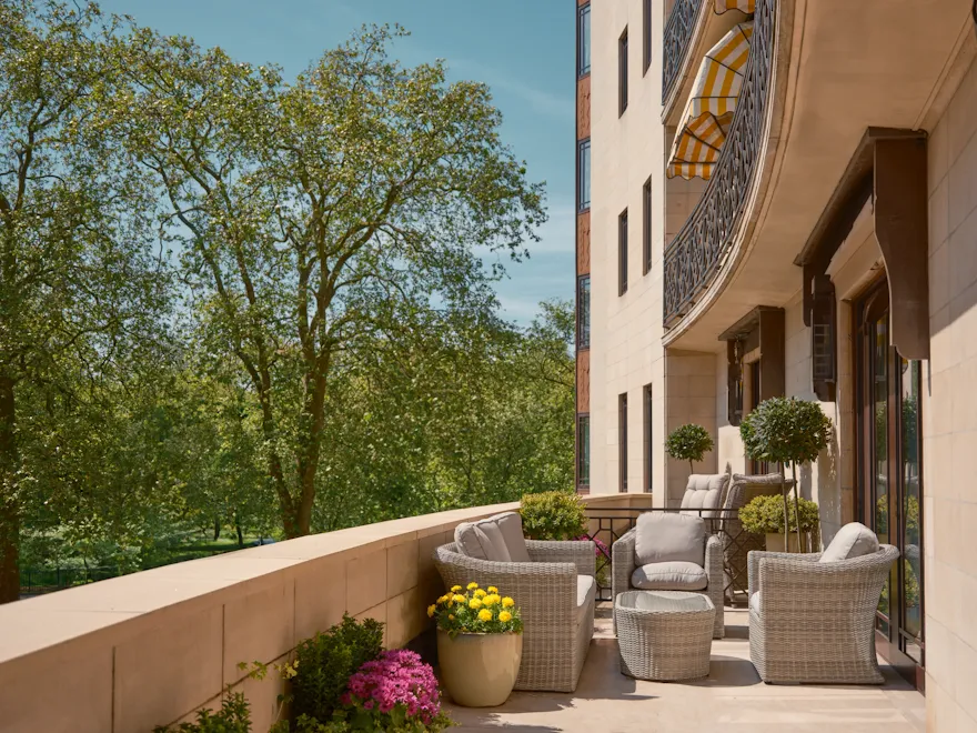 Spacious private terrace at The Dorchester’s Garden Terrace Suite, with woven armchairs and tables arranged for outdoor relaxation, framed by colourful potted flowers and overlooking a tranquil canopy of trees on a bright summer day.