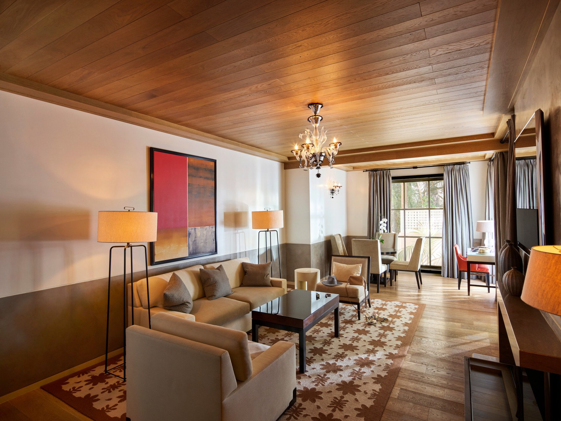 Living room set, artwork, door to private patio, dark and rich colors with pop of reds and elegant chandelier in the Grand Suite at Hotel Bel-Air