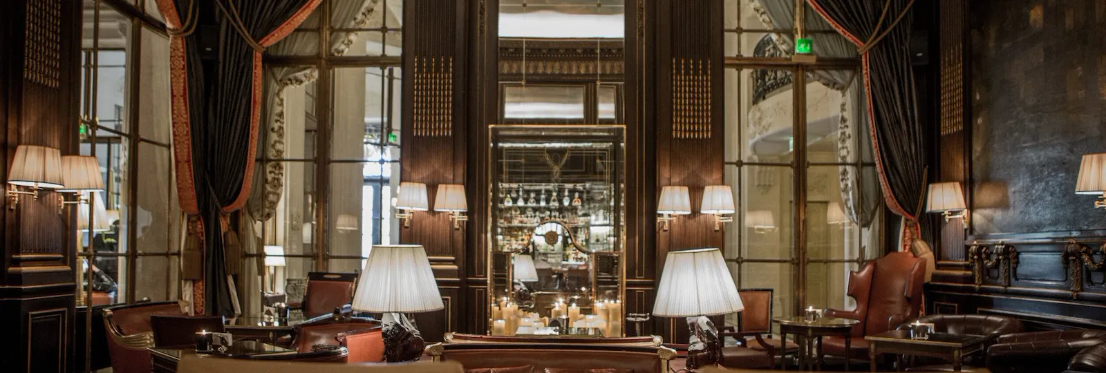 Tables basses et chaises, bougie et miroirs à l'arrière-plan de la photo reflétant les étagères en verre du bar, au Meurice, Paris.