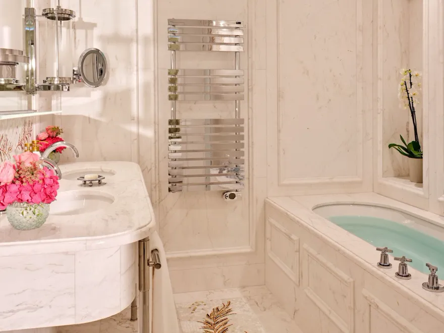 Salle de bains élégante aux surfaces en marbre, avec un meuble-lavabo blanc orné de fleurs, un porte-serviettes chromé et une baignoire décorée d'orchidées, respirant le luxe.