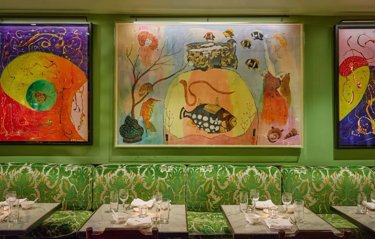 Interior dining space at China Tang at The Dorchester, showcasing colourful contemporary artworks displayed against green walls, patterned upholstered banquette seating and tables set with fine tableware and glassware.