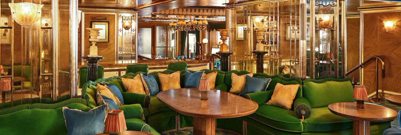 Curved green banquette seating and wooden tables at The Vesper Bar, set within warm Art Deco interiors.