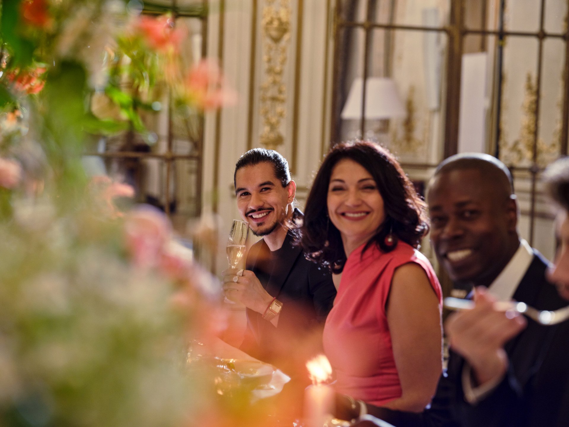 Des convives rient à table, regardant l'objectif de l'appareil photo, lors d'un dîner au Salon Pompadour de l'hôtel Le Meurice, Paris - Dorchester Collection.