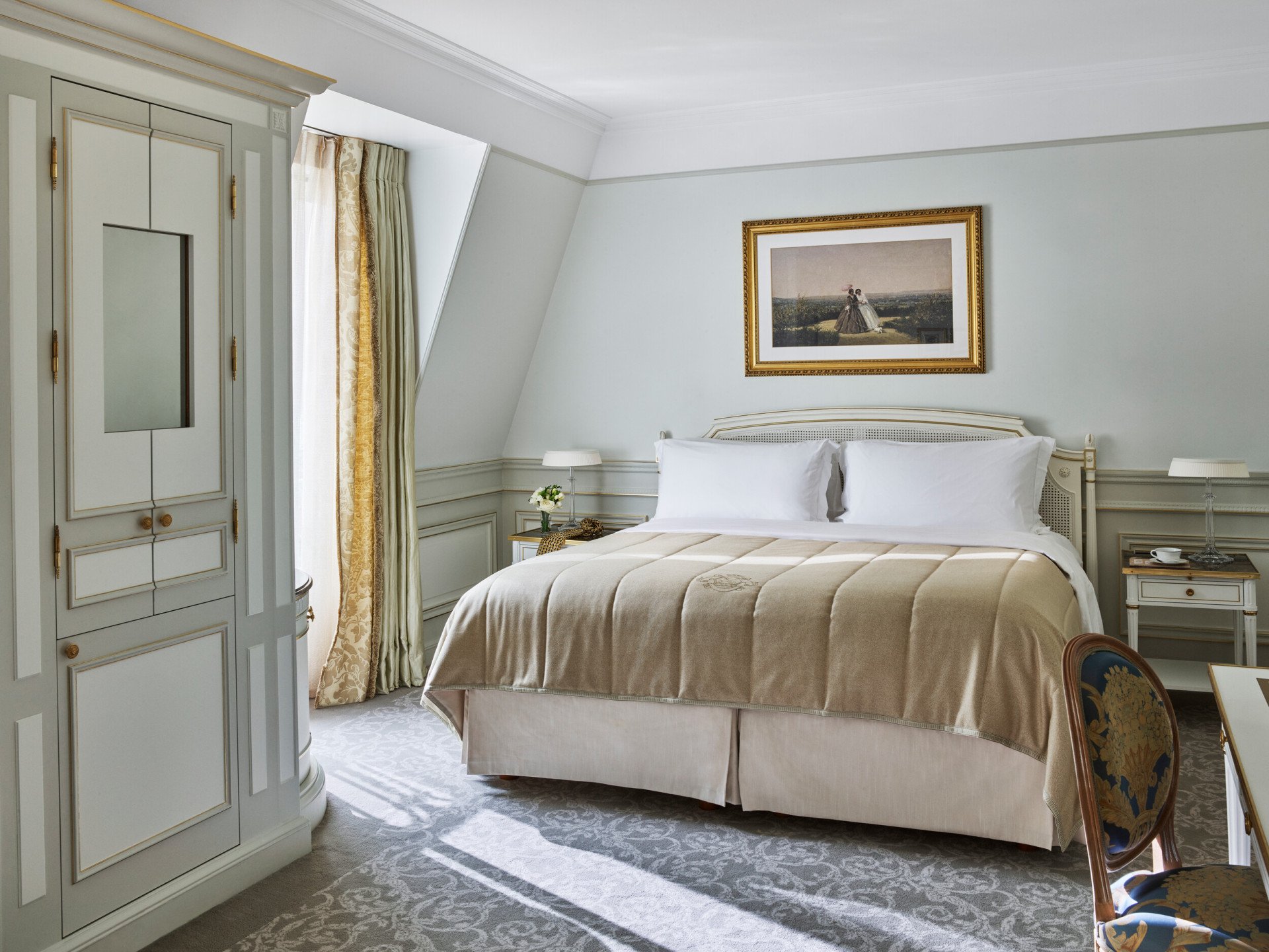 Chambre d'hôtel luxueuse avec un lit king-size soigneusement fait, des draps beiges, d'élégants murs bleu clair, un tableau encadré au-dessus et un éclairage tamisé.