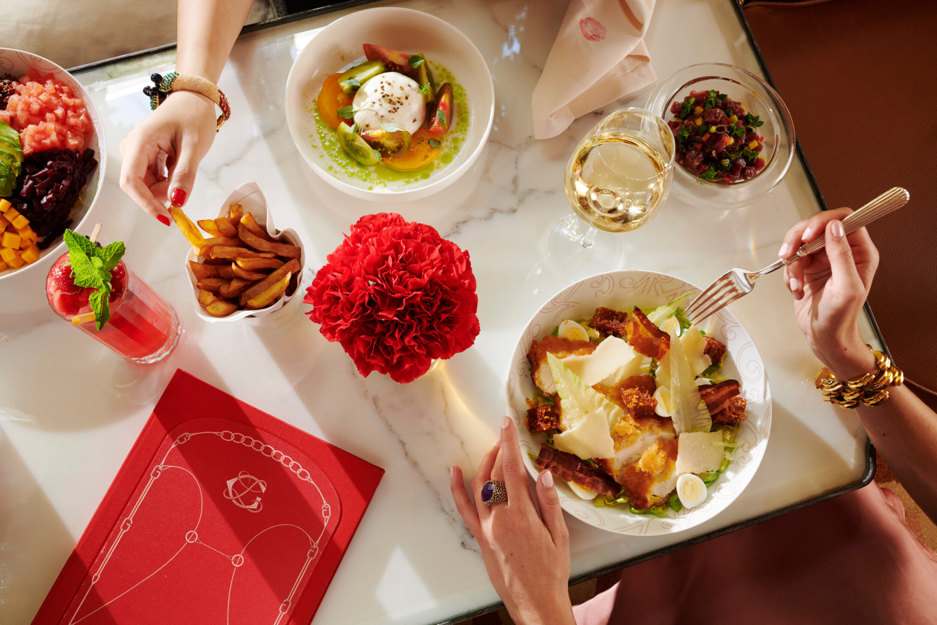 Mulheres almoçando na La Galerie, olhando de suas mãos colhendo batatas fritas e comendo uma salada caesar, McCarthy Salad e vinho branco na mesa, no Hotel Plaza Athénée, Paris