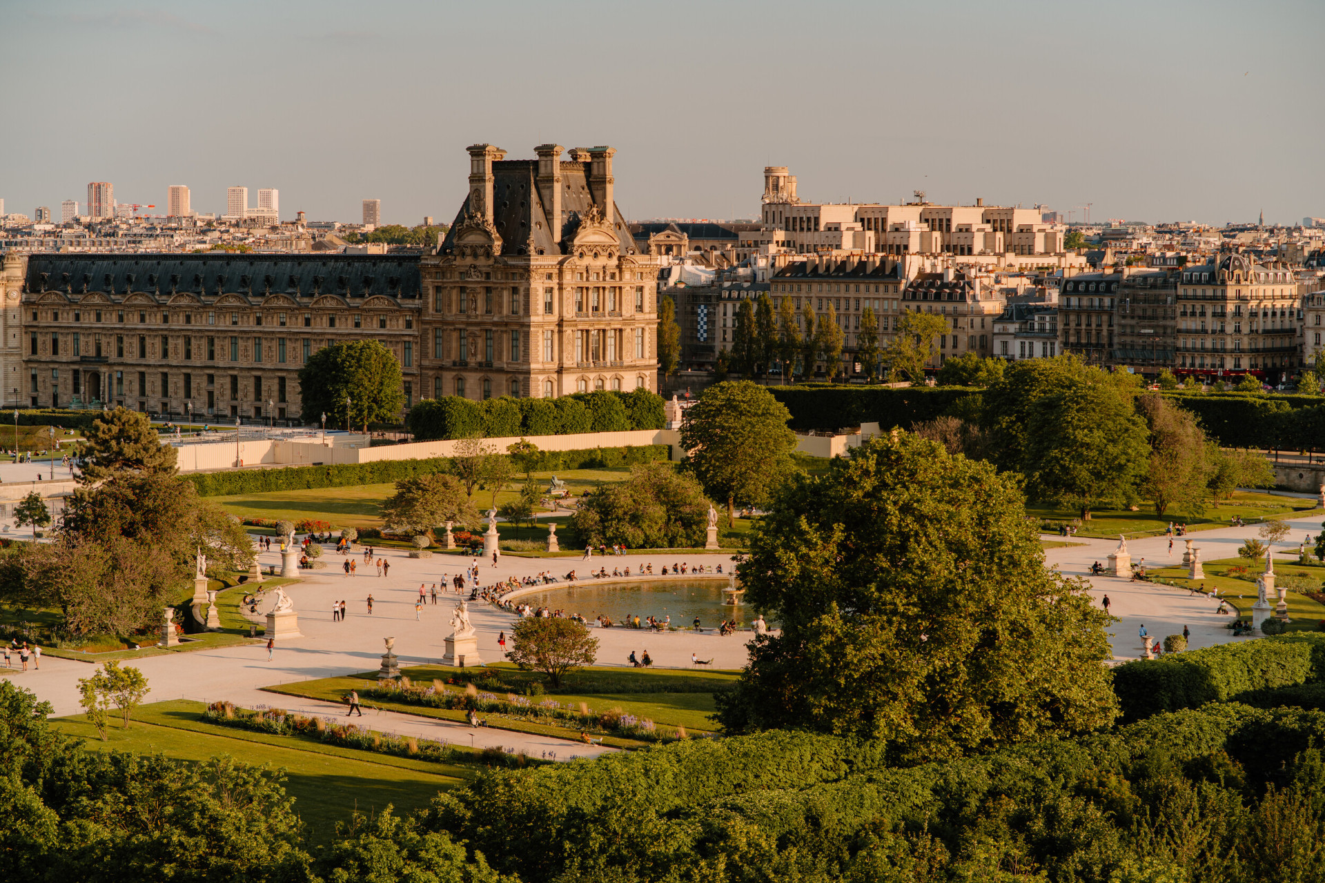 Vue aérienne des jardins des Tuileries avec une lumière jaune lisse, au coucher du soleil. Un étang avec une fontaine et des chaises autour est au centre de l’image, au jardin des Tuileries, Paris  