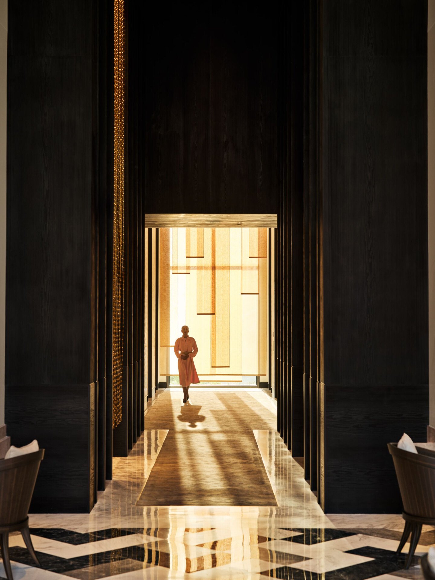 Staff member in pink dress walking through lobby corridor in morning light at the Lana Dubai