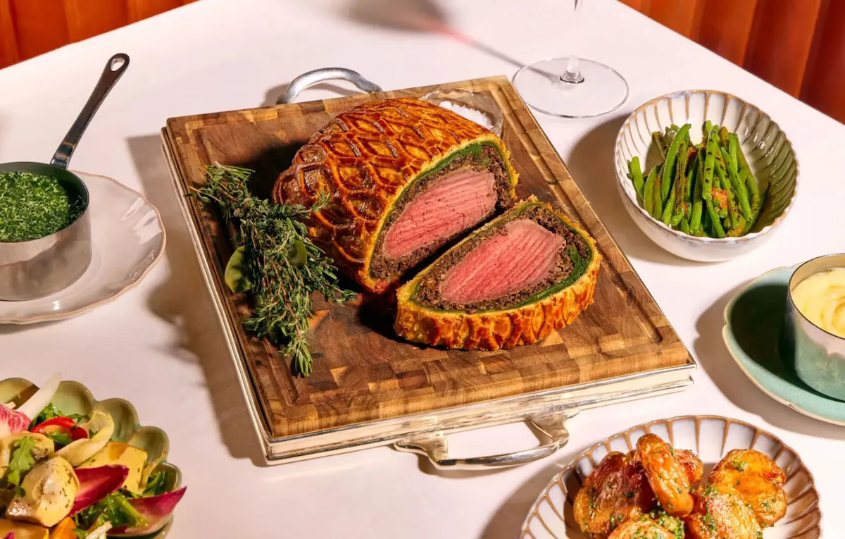 Dining table at The Grill at The Dorchester, showcasing a Beef Wellington sliced to reveal a pink centre, served with asparagus, creamed spinach, roasted potatoes and a fresh seasonal salad.