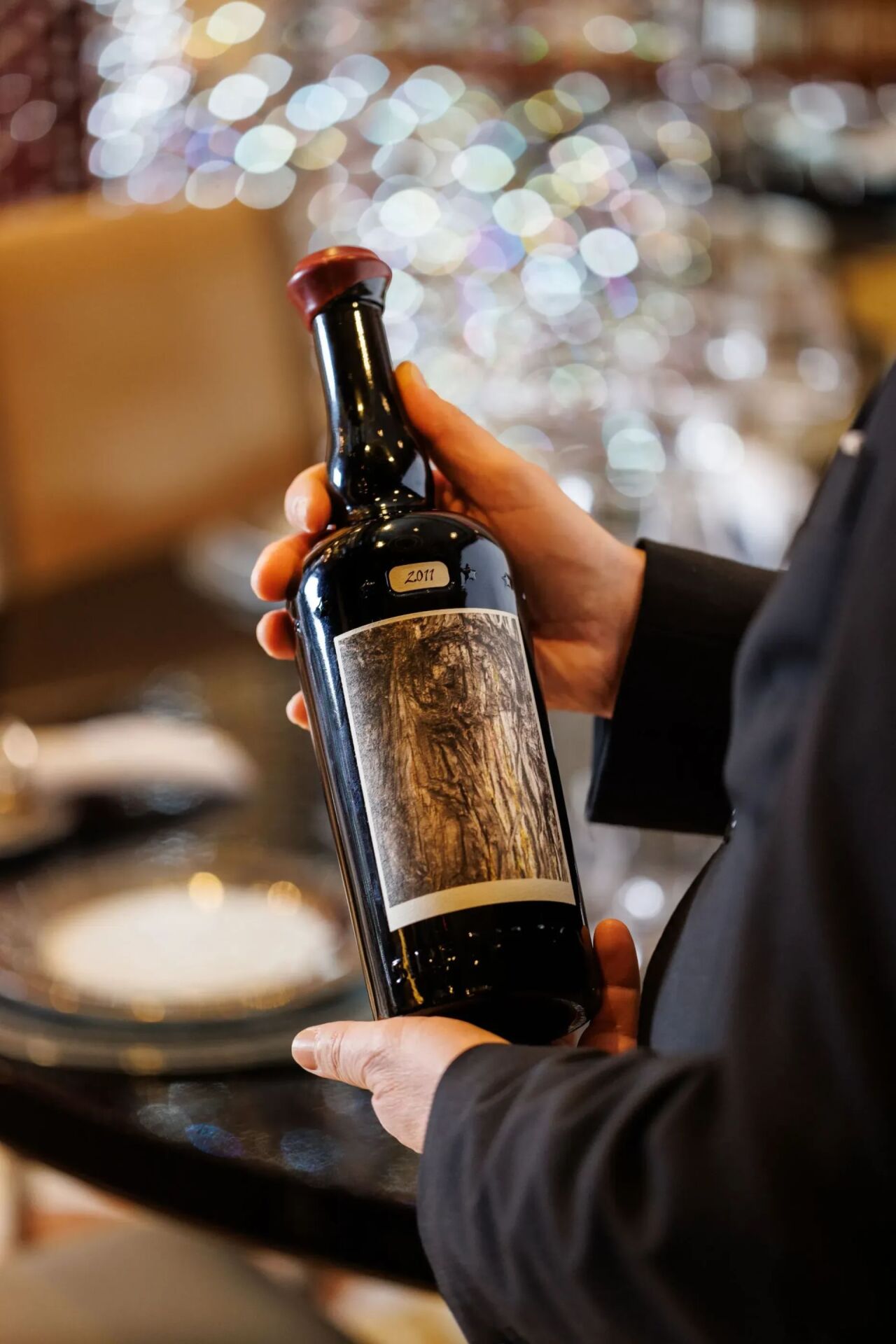 Una delle nostre bottiglie della selezione 'I grandi vini del mondo' sorretta dal sommelier, sullo sfondo il tavolo cristallo 