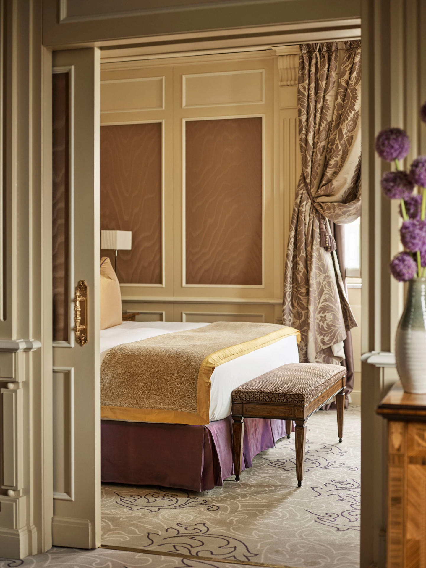 Camera da letto della Suite Ambassador, immagine che rivela il letto king size e un bouquet di fiori viola