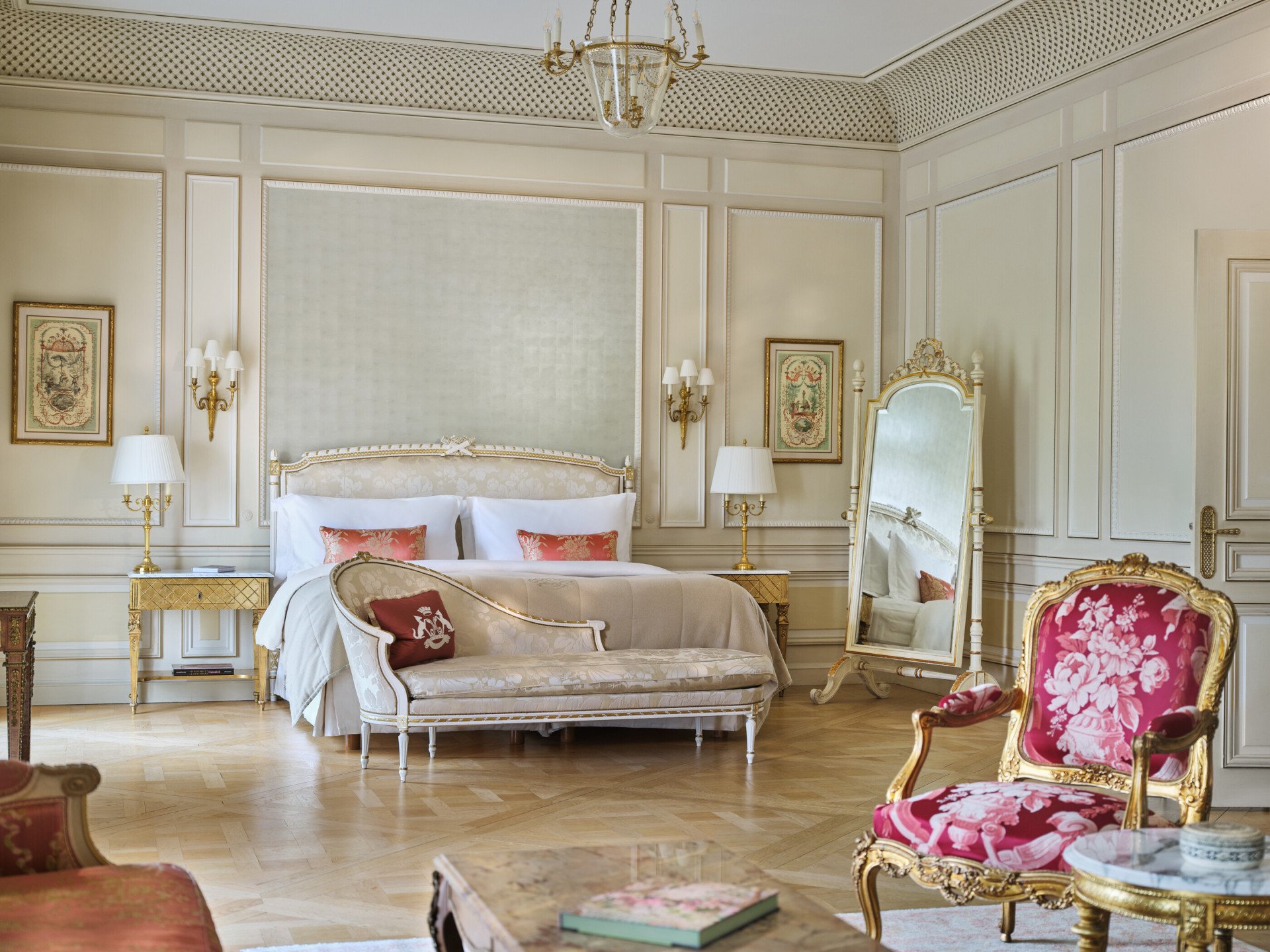 Vista ampla de uma Suíte Versalhes com a cadeira e a mesa em primeiro plano e o sofá, a cama e o espelho ao fundo, no Le Meurice, Paris