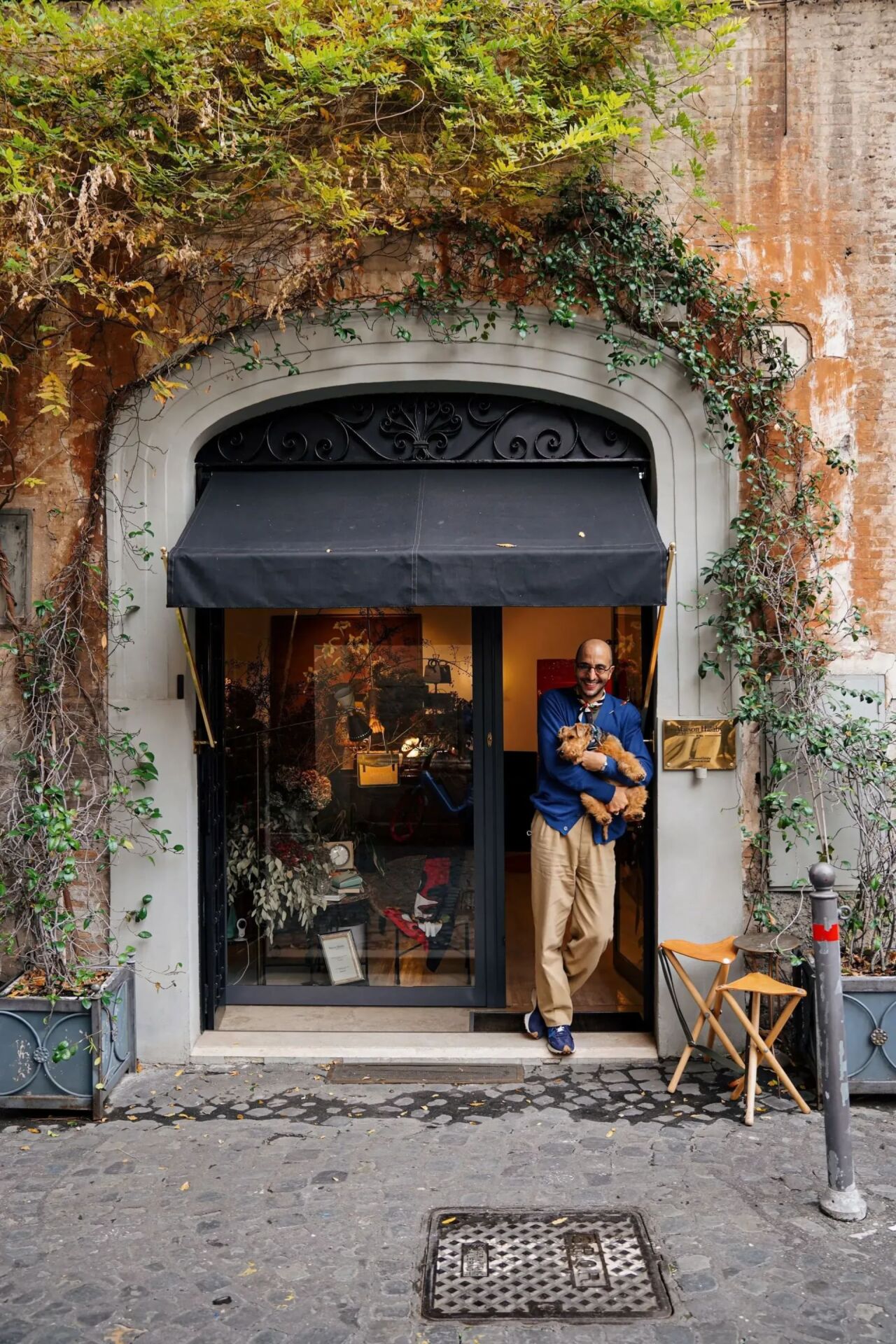 Man standing at the entrance of a shop holding a small dog in his arms