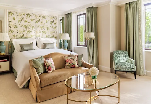 The Executive Park View Room at The Dorchester, showcasing botanical-patterned wall coverings, a king-sized bed, a comfortable seating area, green accent furnishings and large windows overlooking Hyde Park.