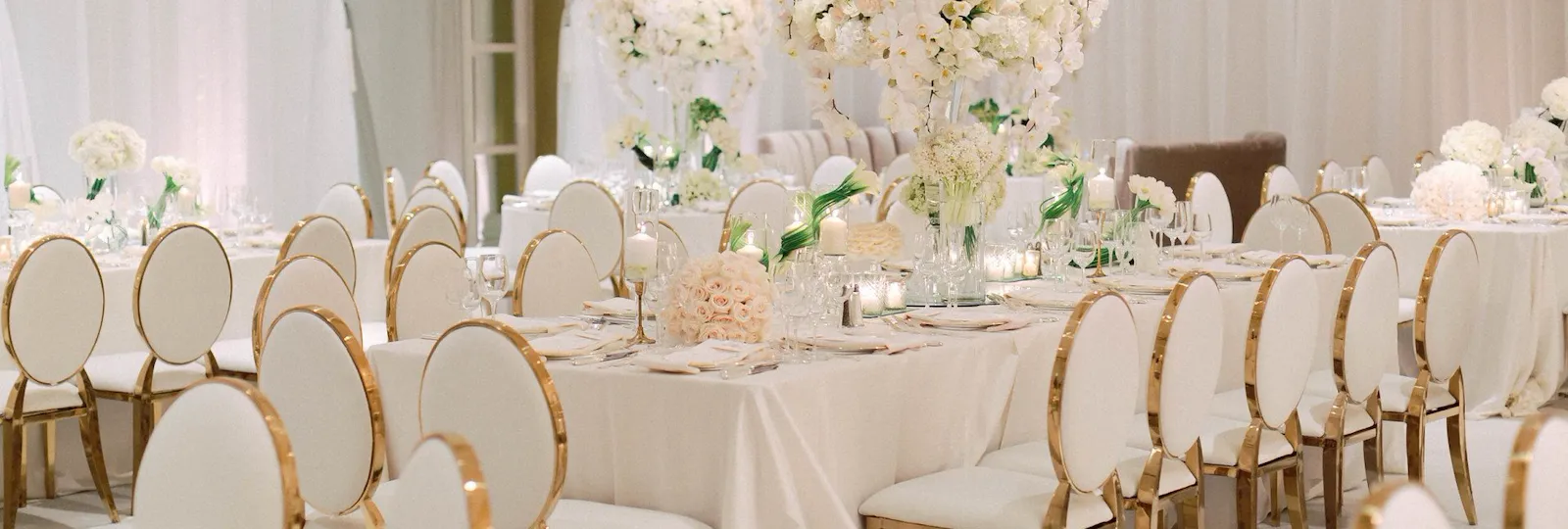 Elegant all white table setting with floral centerpieces and gold lined chairs in the Crystal Ballroom