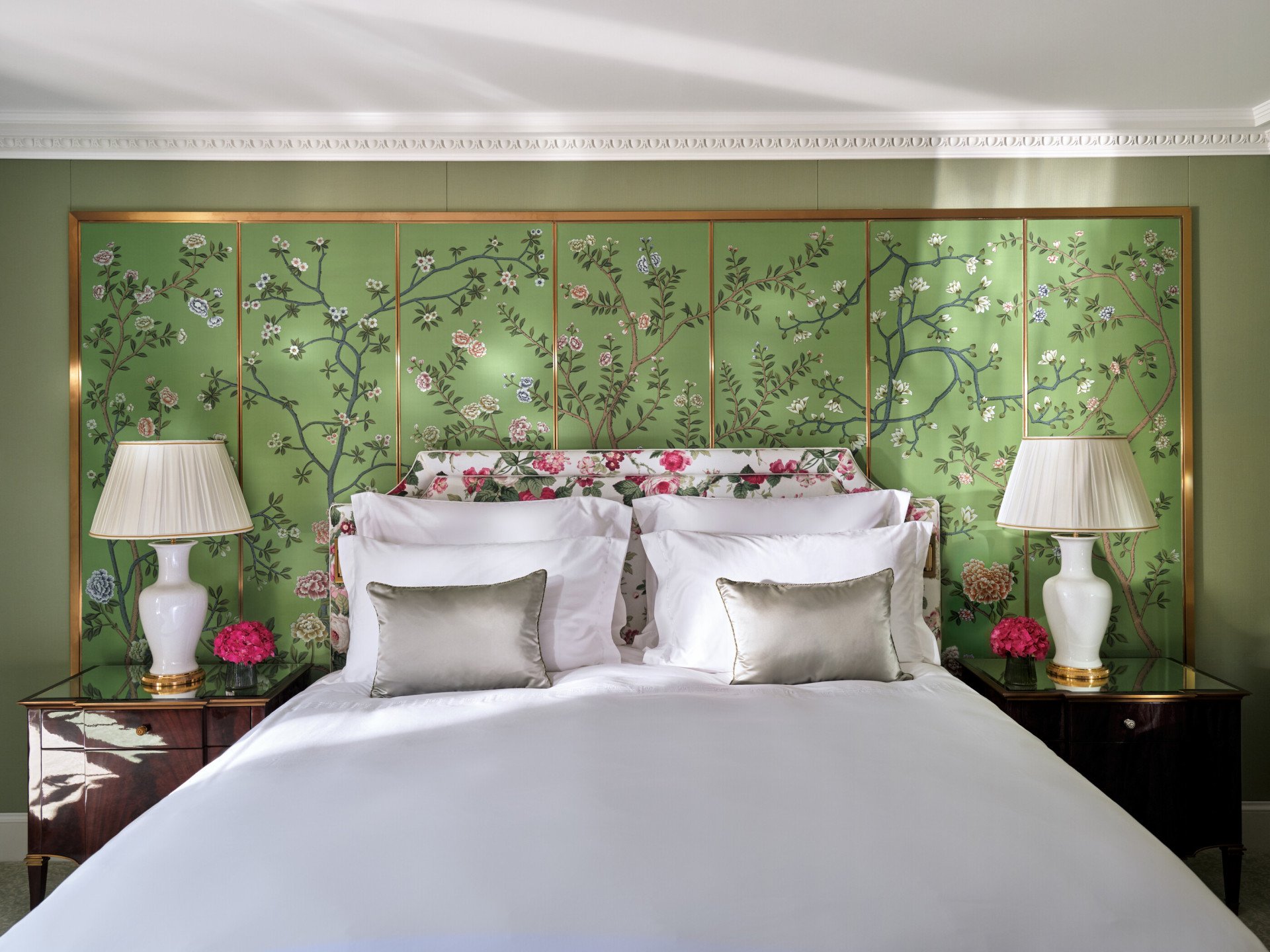 The Belgravia Suite bedroom at The Dorchester, featuring a king-sized bed set against a green wall adorned with an elegant hand-painted floral mural, complemented by bedside lamps and glossy wood furnishings.