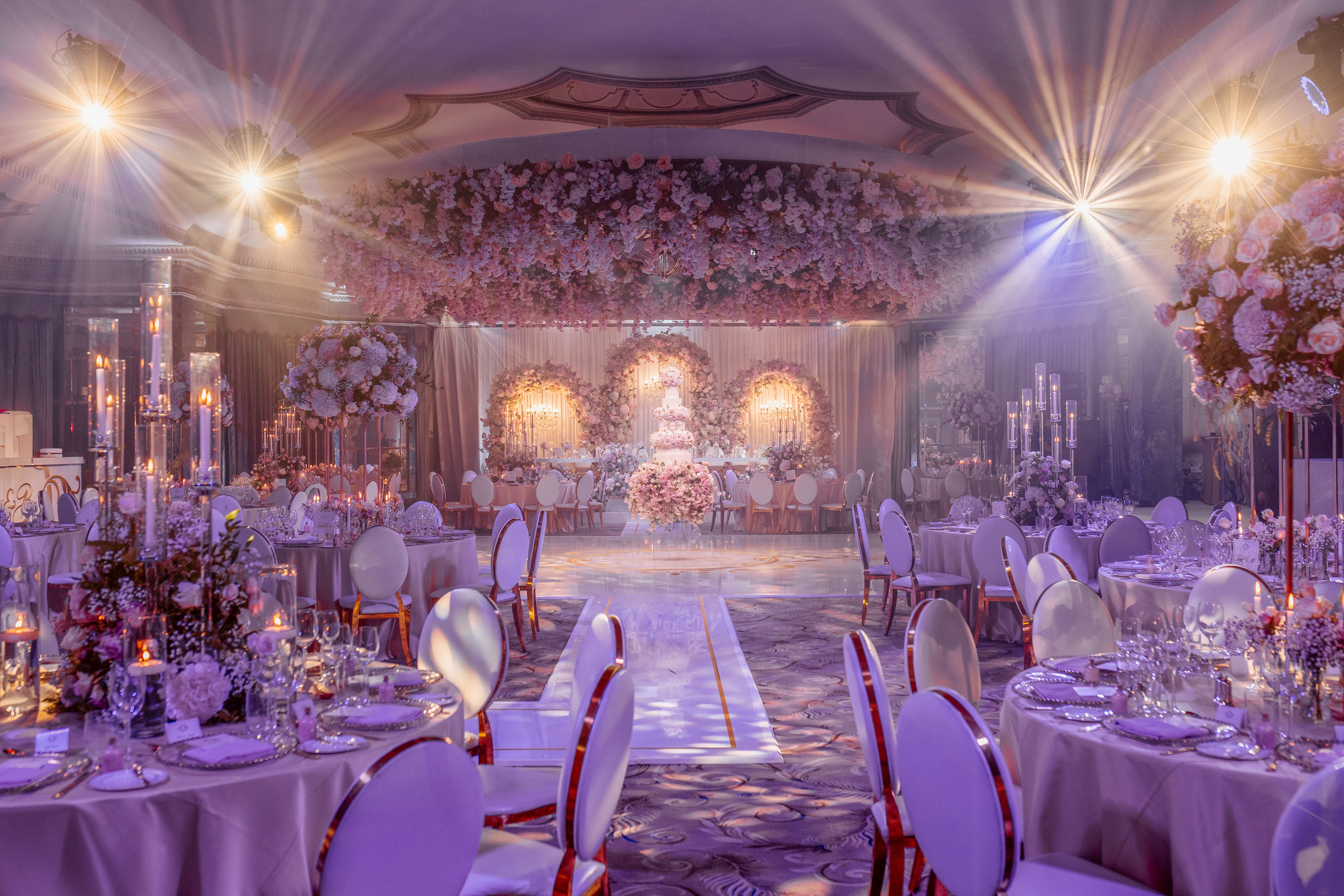Extravagant wedding set-up in the ballroom with pink and white floral arrangements, 3 tier cake, dance floor and tables