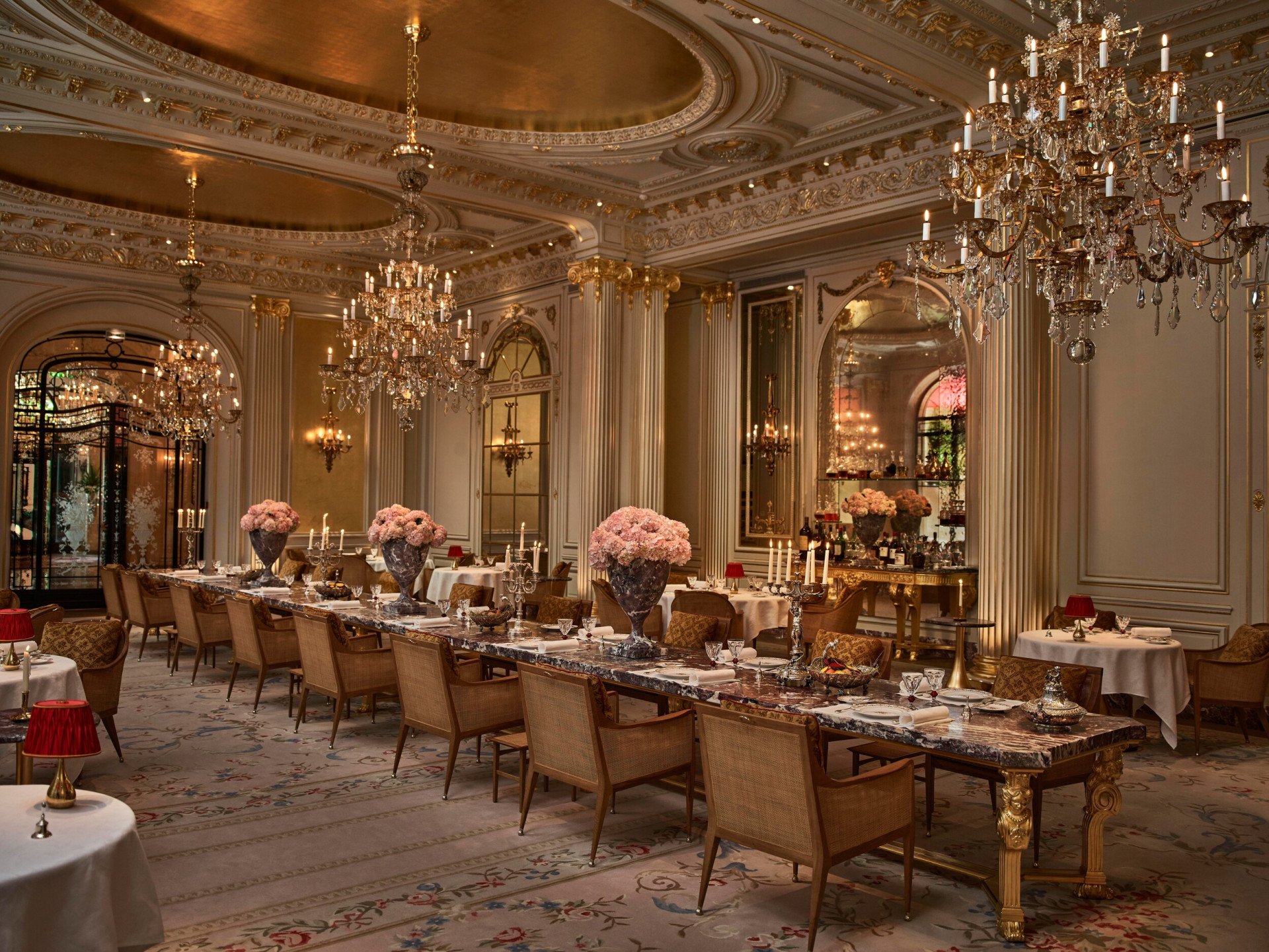 Vue d’ensemble du restaurant Jean Imbert au Plaza Athénée et sa table centrale en marbre avec des fleurs et des lustres en cristal suspendus au plafond. À l’Hôtel Plaza Athénée, Paris