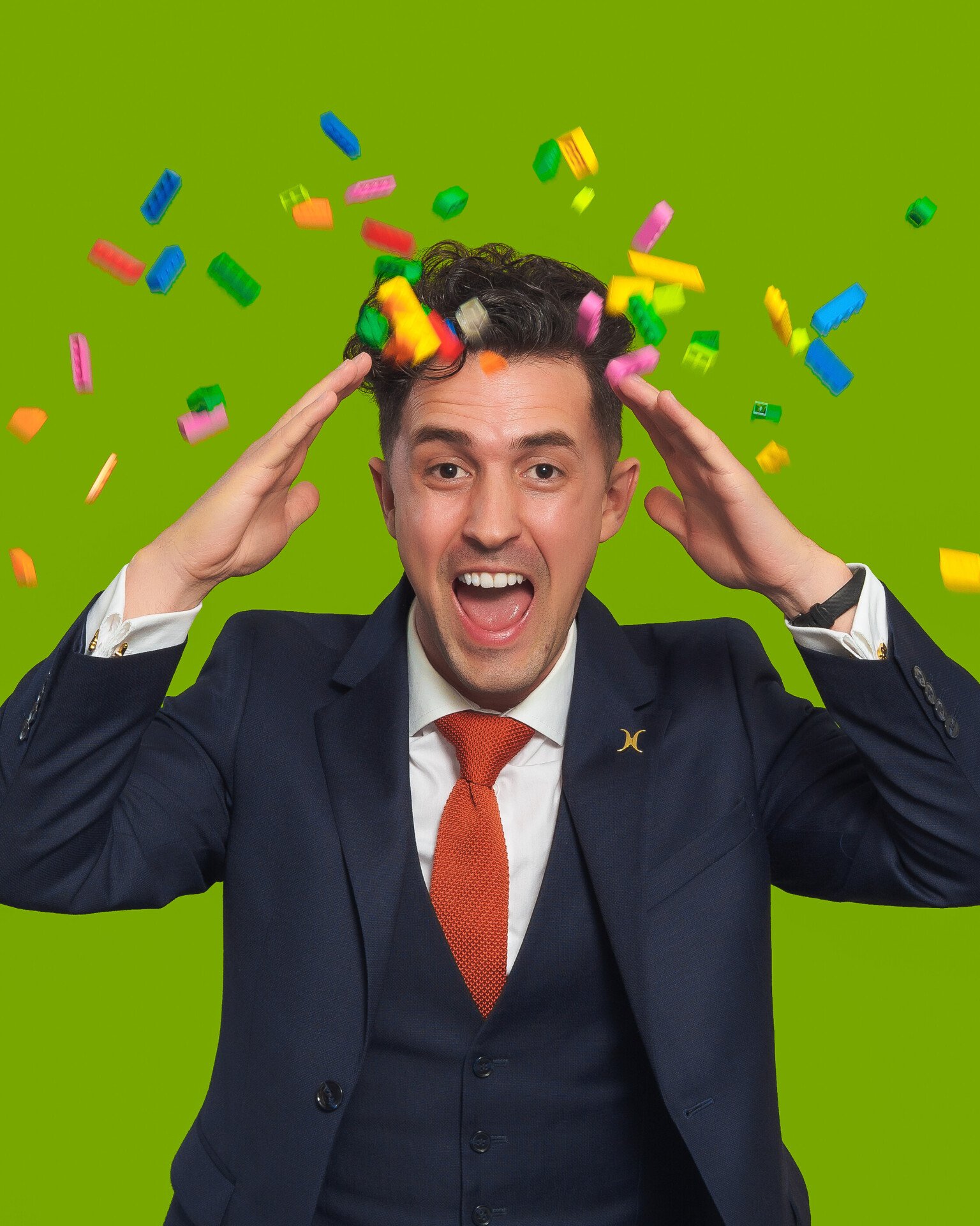 Man against green background with lego pieces flying around his head 