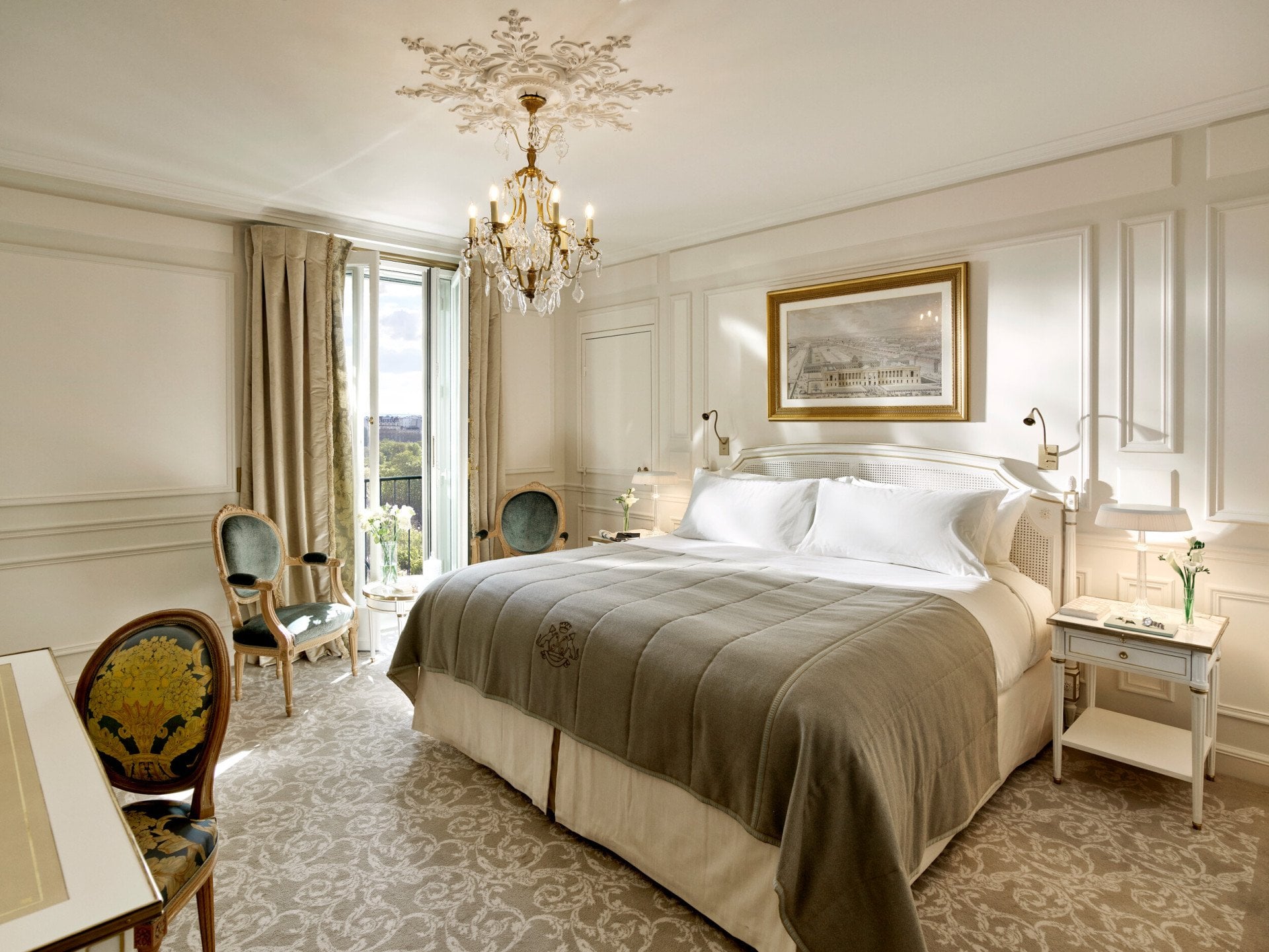 Vue globale d'une chambre exécutive mettant en valeur les tons gris clair et crème, ainsi que la vue sur le jardin des Tuileries en arrière-plan. Bijoux et livres sont sur les tables de chevetAu Meurice, Paris.