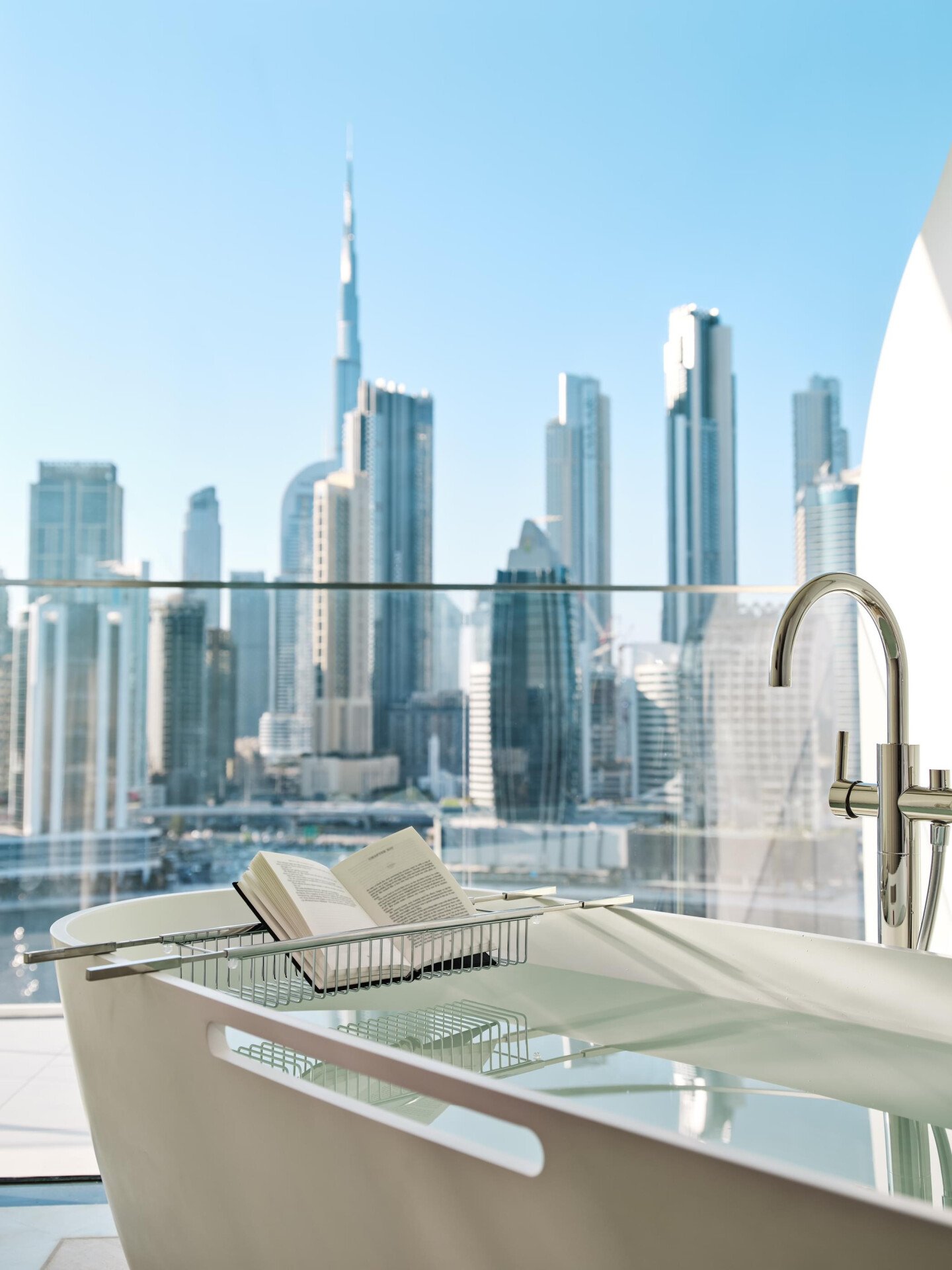 The Suite's bathtub with a book in the stand with Dubai's skyline in the background