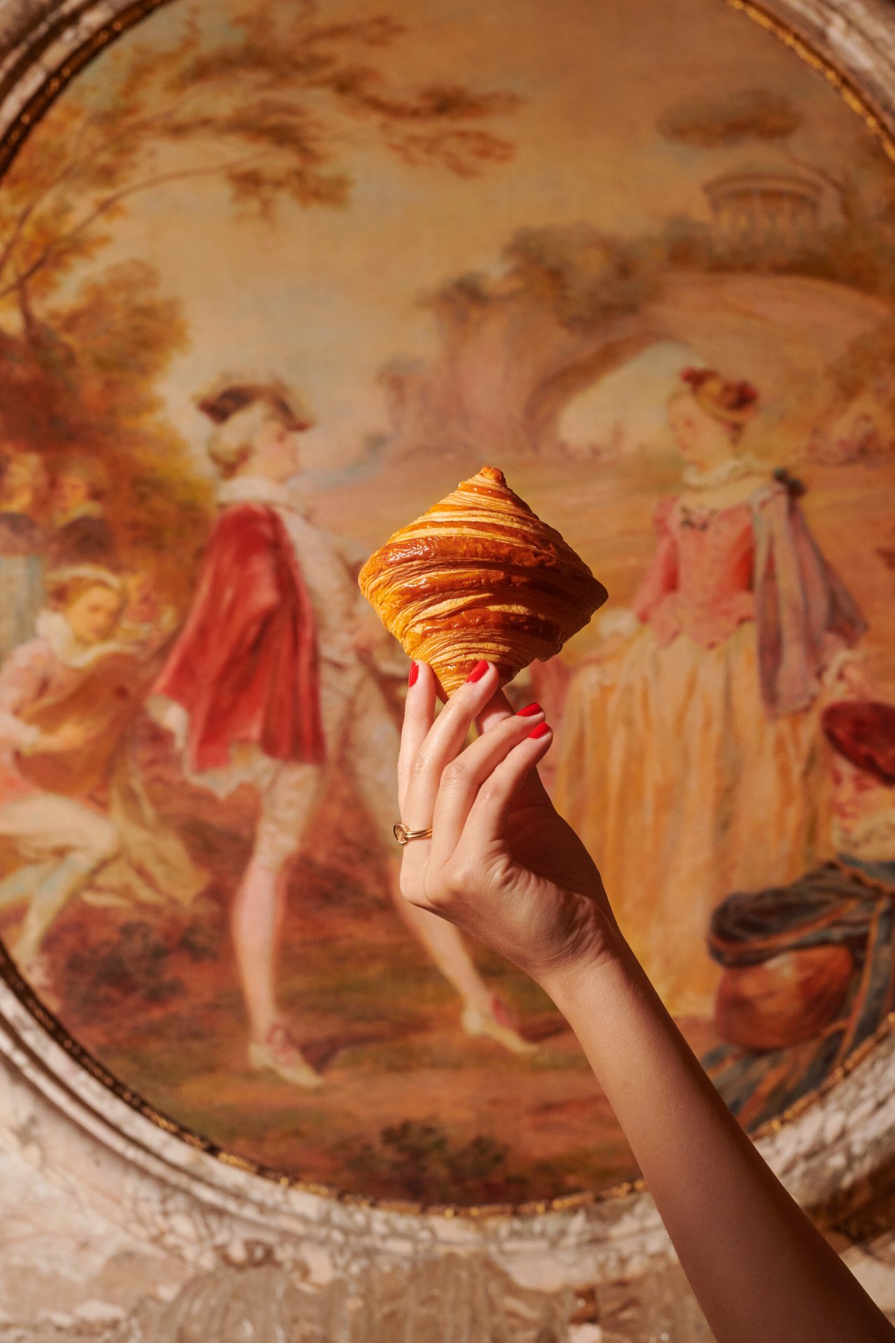 Mão segurando um croissant em frente a uma pintura no Le Meurice, Paris - Coleção Dorchester