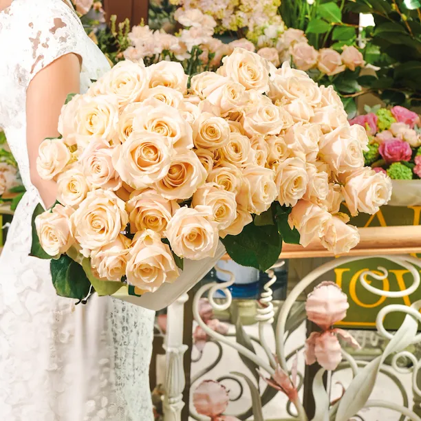 Woman holding large bouquet of soft blush Dorchester roses in Cake and Flowers boutique