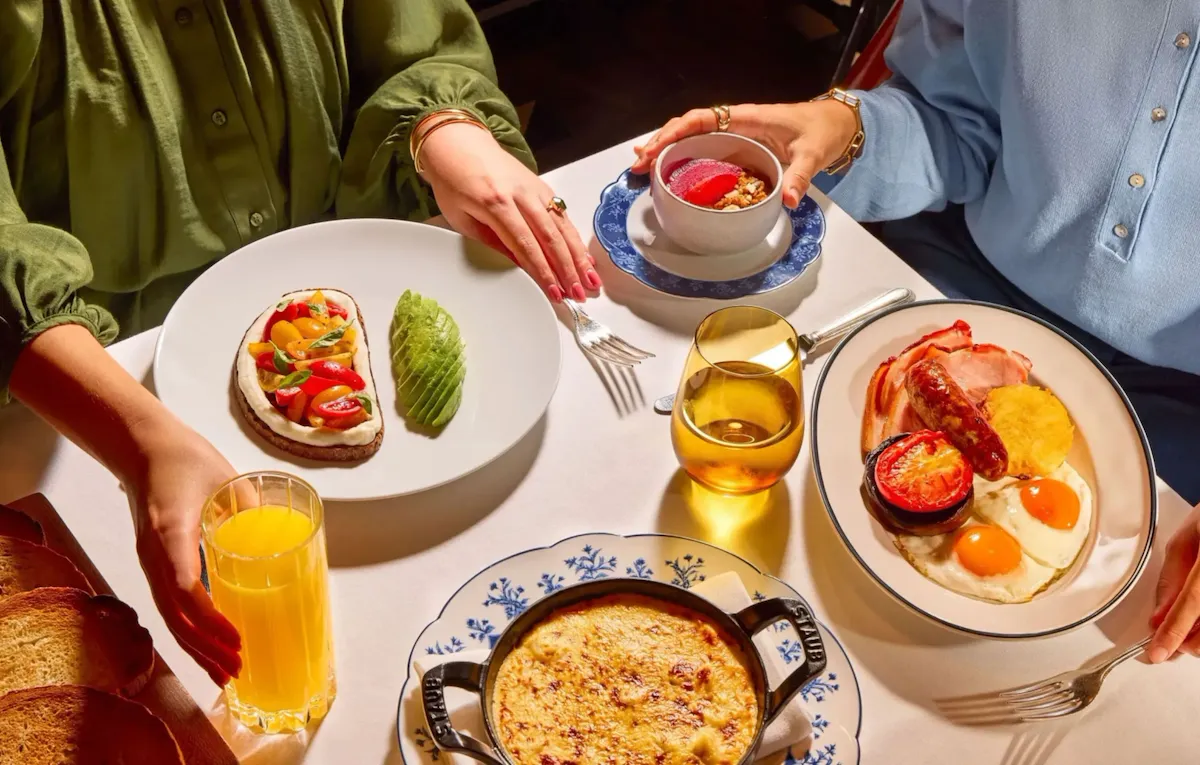 Dining table at The Grill at The Dorchester, showcasing a selection of breakfast and brunch dishes including tomato on toast with basil, eggs and bacon, a baked gratin-style dish, fresh berries and glasses of orange juice.