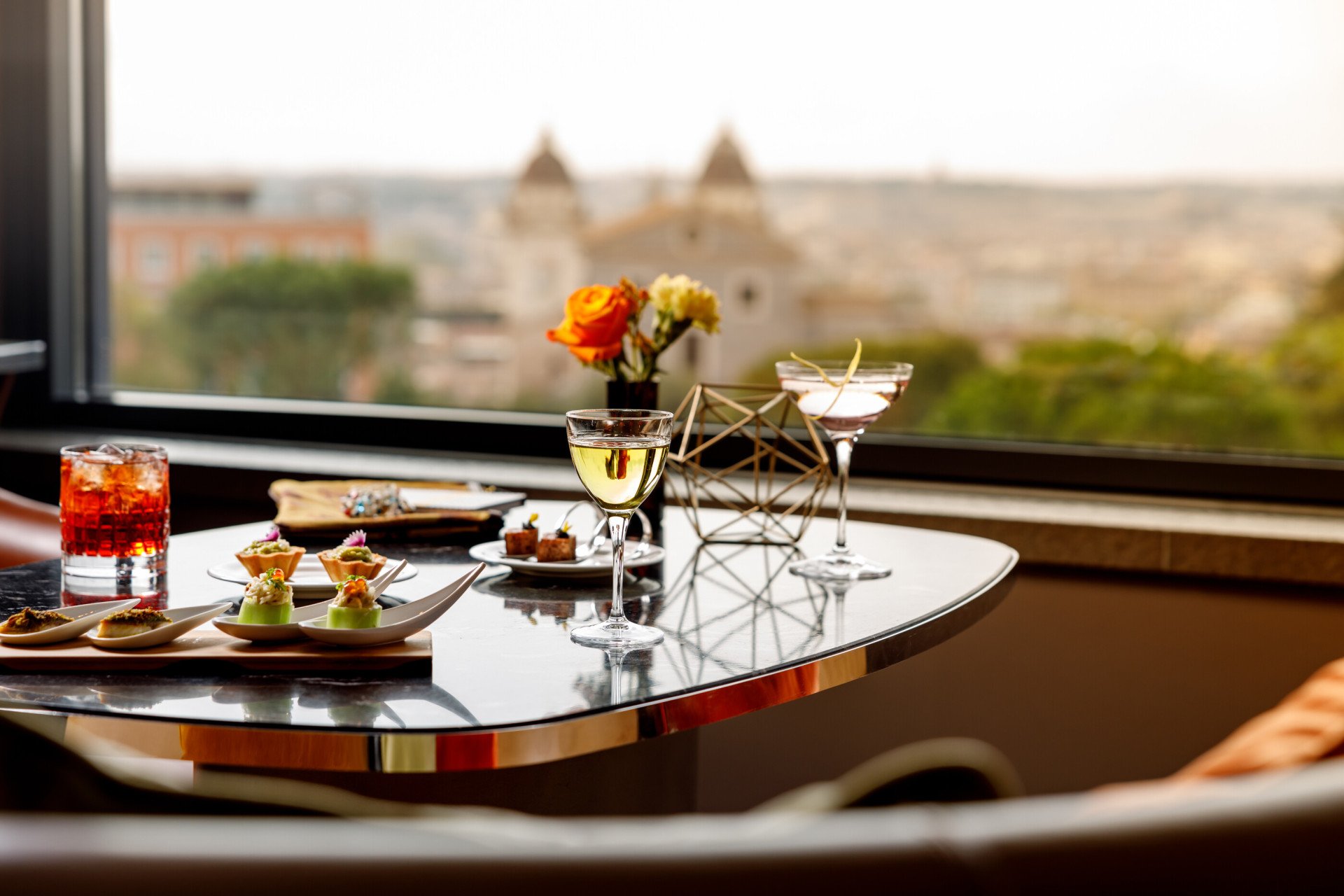 Tre cocktail e vari canapes su di un tavolo con vista su Roma a Il Giardino Bar
