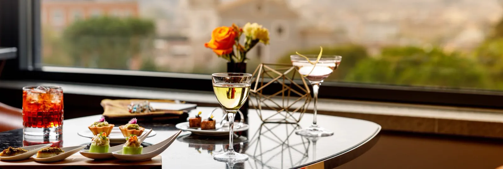 Tre cocktail e vari canapes su di un tavolo con vista su Roma a Il Giardino Bar