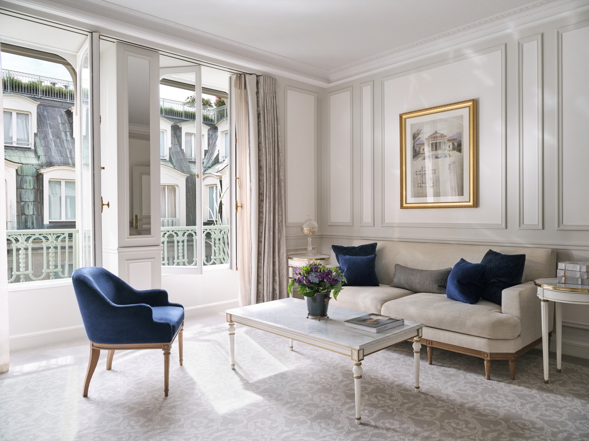 Salon d’une suite de luxe avec une chaise, une peinture au-dessus du canapé et une table avec des fleurs et des livres sur le dessus, au Meurice, Paris