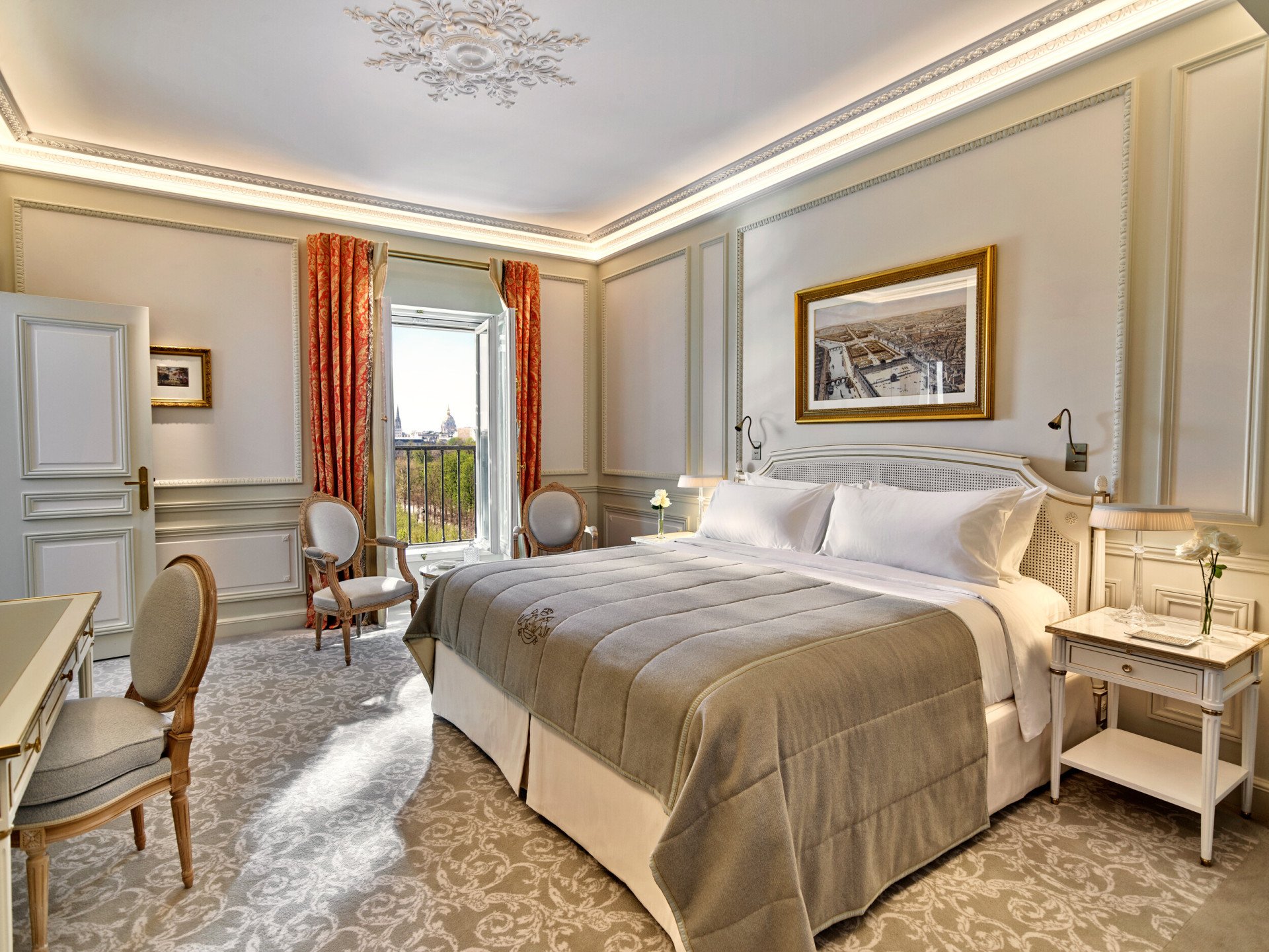 Quarto de hotel luxuoso com cama macia, cadeiras elegantes e janela aberta com vista panorâmica. O quarto tem decoração ornamentada e tons quentes e acolhedores.