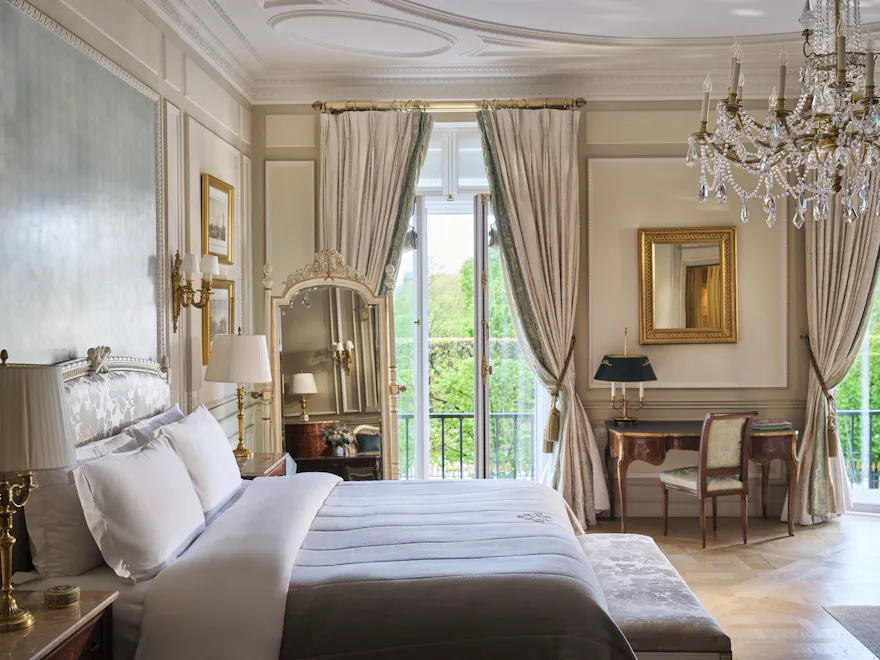 Large view of the right side of the bed with the mirror, the desk, the chair and the windows open behind, at Le Meurice, Paris